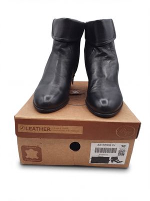 des bottines en cuir noir posées sur une boîte en carton, sur fond blanc