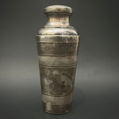 un vieux vase en argent posé sur une surface grise