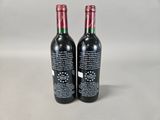 two bottles of red wine sitting on top of a table