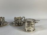 two silverplated tea cups and saucers on a white table