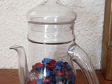 une théière en verre remplie de billes, posée sur une table