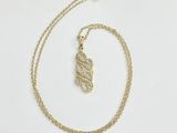 a close up of a gold necklace with a leaf on it