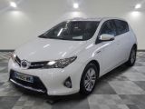 La Toyota Corollant est garée dans une grande pièce au sol carrelé en damier.