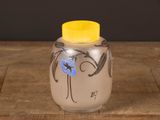 a small glass vase with a yellow lid on a wooden table