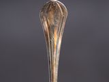 an antique silver spoon with a long handle on a black surface