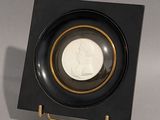 une assiette noire bordée d'or, dans laquelle se trouve une pièce de monnaie