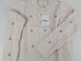 cream cable knit sweater with blue buttons and a tag on the chest