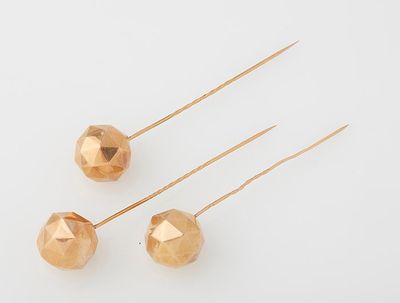 three gold plated metal balls on a white surface with a pair of needles