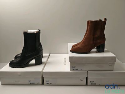 Deux paires de bottes sont posées sur des cartons, sur une table.