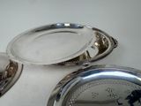 two silver trays sitting on a table with a clock in the background