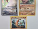 Trois cartes Pokémon sont représentées sur une surface blanche