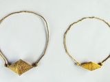 two gold hoops with small beads on them on a white surface