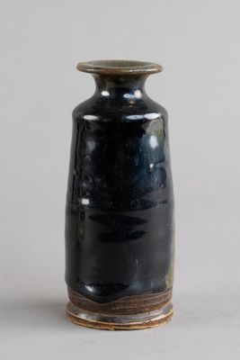 un vase noir surmonté d'un couvercle en bois, posé sur une table