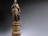 une statue en bronze représentant une femme tenant un enfant dans ses bras, posée sur un socle