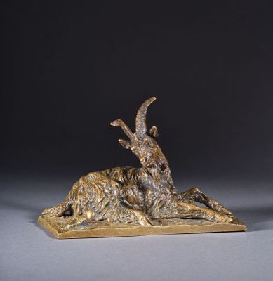 une sculpture en bronze représentant une chèvre couchée sur un socle en bois