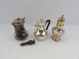 three silver teapots and a wooden spoon on a white surface