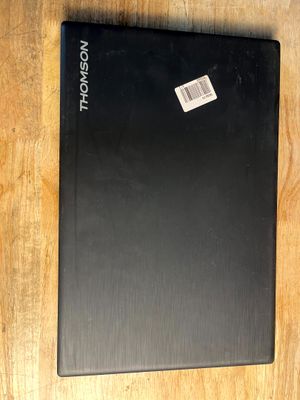 un ordinateur portable noir posé sur une table en bois, sur laquelle est collé un autocollant