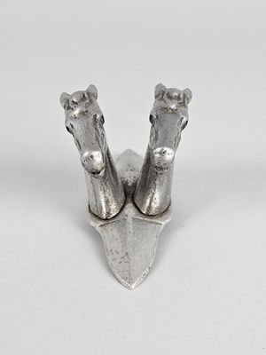 paire de figurines en métal argenté représentant des têtes de cheval, posées sur un support blanc