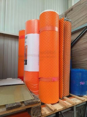 Plusieurs rouleaux de filet orange sont empilés sur des palettes dans un entrepôt