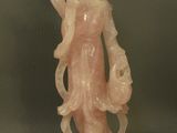 une statue en jade rose représentant une femme tenant un oiseau, posée sur un socle en bois