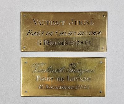 deux plaques en laiton posées sur un fond blanc, sur lesquelles figurent les noms de deux personnes