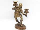 brass figurine of a man holding two candles on a pedestal