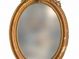 an oval mirror with a gold frame and a flower decoration