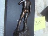 une statue représentant un homme assis sur un rocher, à côté d'un vase