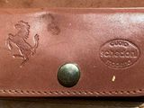 brown leather wallet with a metal button on it sitting on a piece of luggage