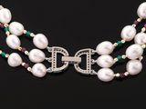 an image of a necklace with pearls and emeralds on a black surface