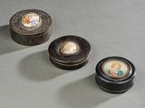 trois petites boîtes noires ornées de photos de personnes, posées sur une table