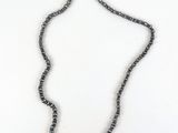 a close up of a necklace on a white surface with a purple flower
