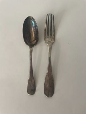 deux cuillères et une fourchette en argent sur une surface blanche