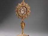 an ornate gold clock on a stand with a cross on top of it