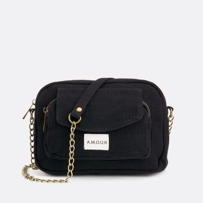 un sac à bandoulière noir muni d'une bandoulière en chaîne et d'une étiquette avec un nom sur le devant