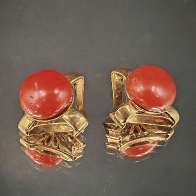 une paire de boucles d'oreilles rouges et dorées posées sur un fond noir