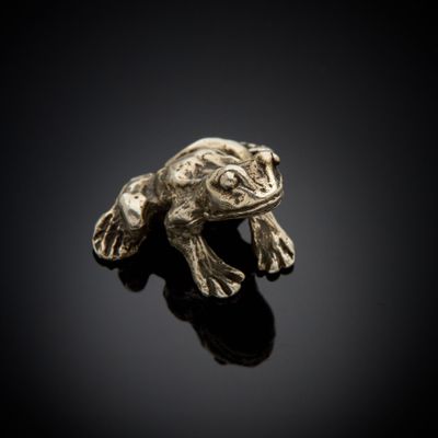 un gros plan d'une figurine de grenouille posée sur une surface noire