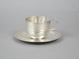 silver cup and saucer with saucer on plate on grey background