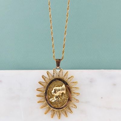 a gold necklace with a gold sunburst on a marble surface