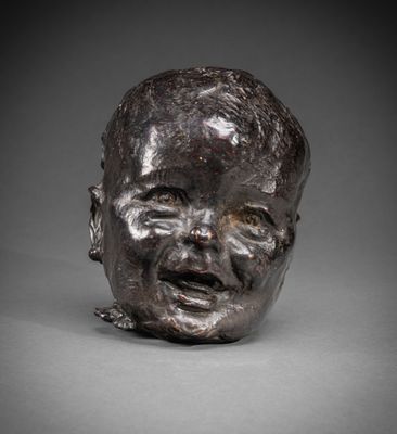 une sculpture en bronze représentant la tête d'un bébé sur une surface grise