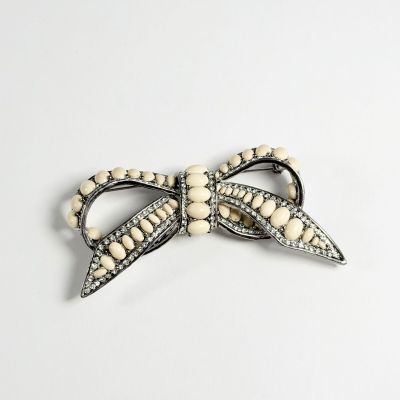une image représentant une broche en forme de nœud blanc ornée de perles