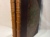 two brown books sitting on top of each other on a white surface