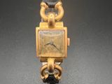 une montre en or, attachée à une chaîne, posée sur un fond noir