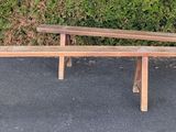 two wooden benches sitting on the pavement near a hedge