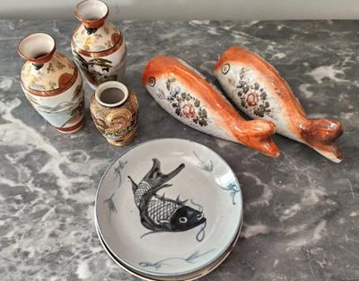 une assiette décorée d'un motif de poisson, à côté de quelques vases et d'une autre assiette décorée d'un motif de poisson