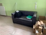a black leather couch in the middle of a room with boxes on the floor