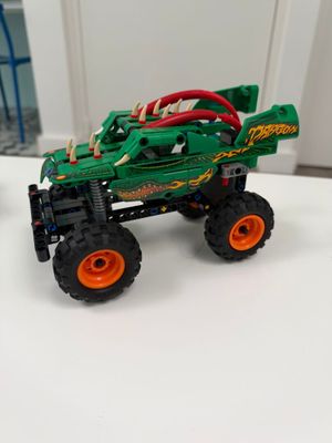 un petit camion jouet vert avec des roues orange posé sur une surface blanche