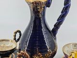 a blue and gold pitcher and cups and saucers