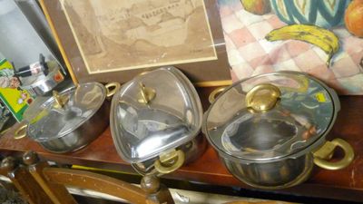 trois casseroles et poêles posées sur une table à côté d'un tableau