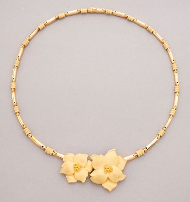 a gold necklace with flowers and beads on a gray background